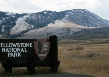 Sign for Yellowstone National Park with snow-dusted mountains in the background.