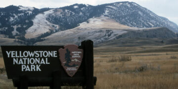 Sign for Yellowstone National Park with snow-dusted mountains in the background.