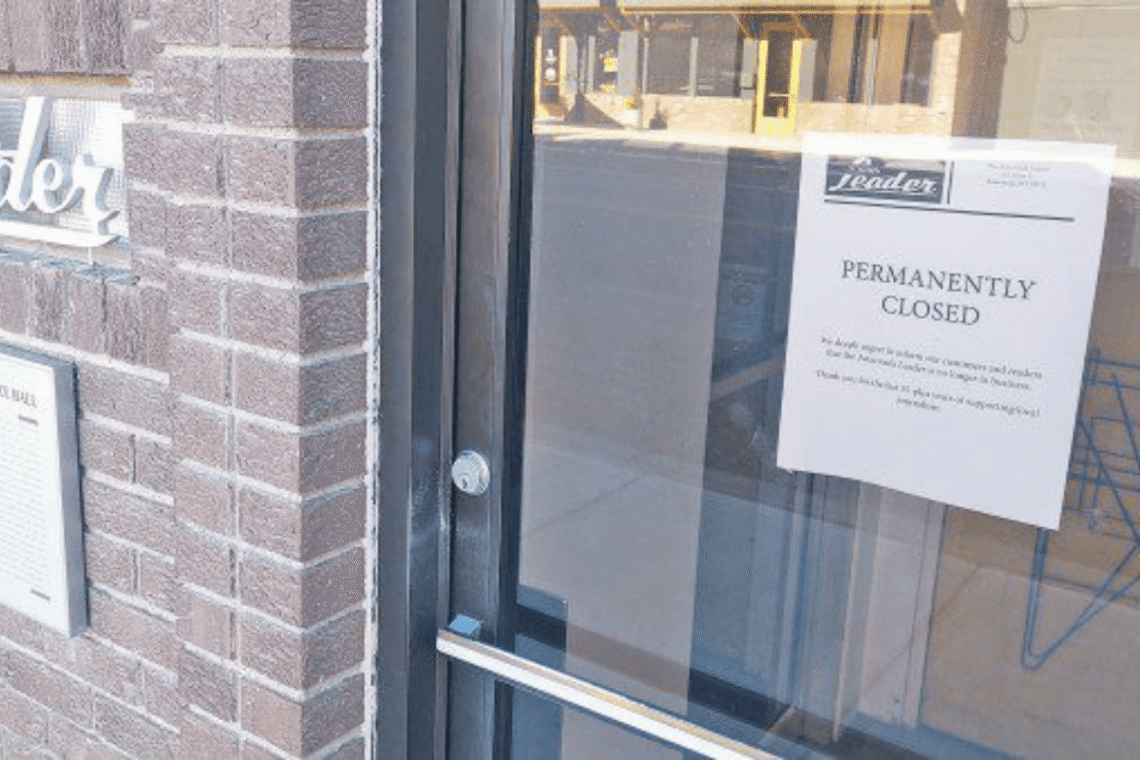 Glass door with a 'Permanently Closed' sign posted on it, brick wall to the left.