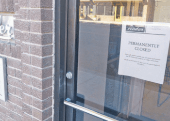 Glass door with a 'Permanently Closed' sign posted on it, brick wall to the left.