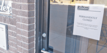 Glass door with a 'Permanently Closed' sign posted on it, brick wall to the left.