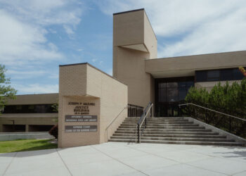 Exterior view of the Joseph P. Mazurek Justice Building with wide concrete steps and railing, beige brick facade, and a prominent sign in the foreground.