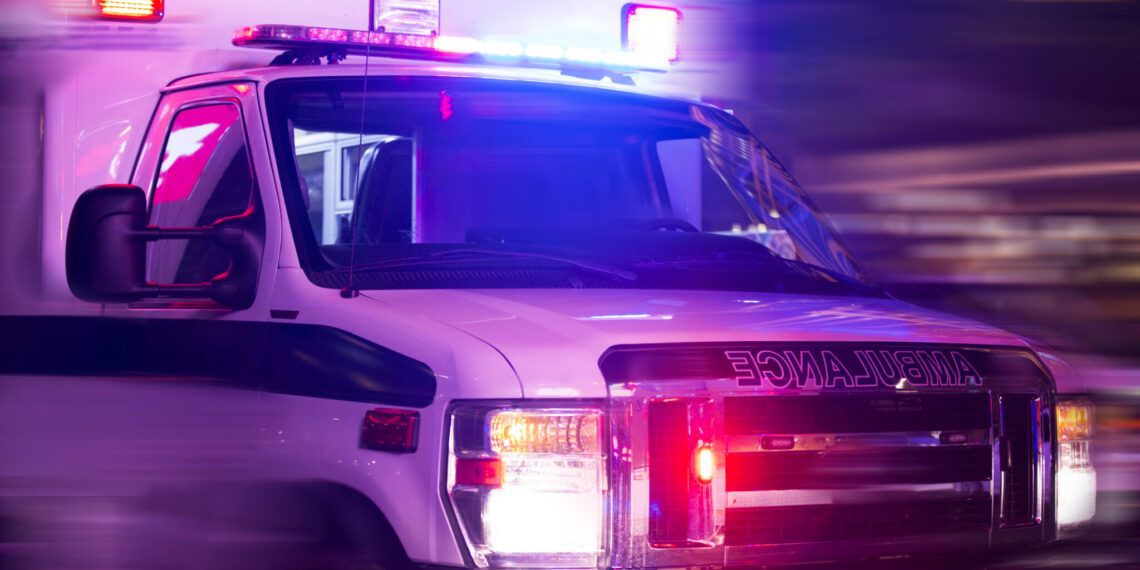 Ambulance rushing by with flashing red and blue emergency lights, motion blur in the background.