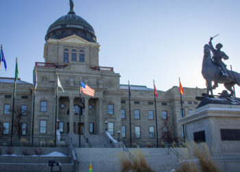 Beige stone capitol building with a large dome, flanked by flagpoles and an equestrian statue in front.