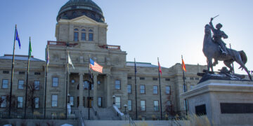 Beige stone capitol building with a large dome, flanked by flagpoles and an equestrian statue in front.