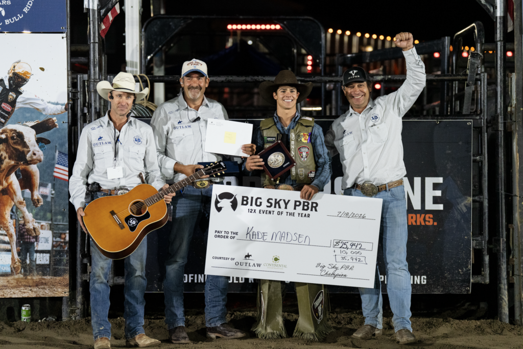 Four rodeo competitors pose on a stage with a giant check for Big Sky PBR Champion, festive banners, and night arena lights behind them.