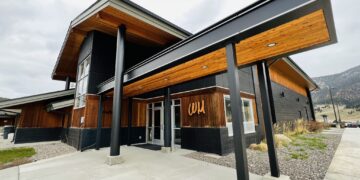 Modern building entrance with wooden panels and dark gray metal beams, mountain landscape in the background