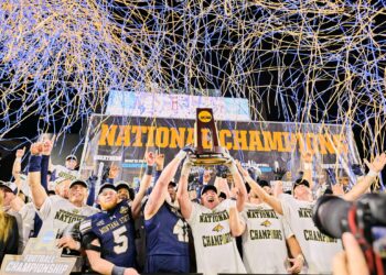Montana State players celebrate a national championship on stage, holding the trophy with blue and gold streamers overhead.
