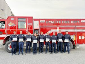 Group of Hyalite Fire Department firefighters in uniform posing with certificates in front of a red fire truck.