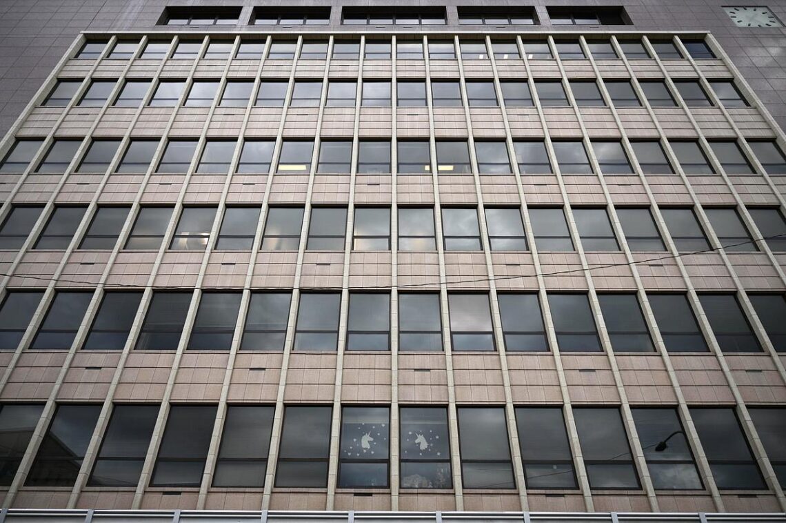 Facade of a modern office building with a grid of square windows framed by vertical and horizontal concrete mullions.