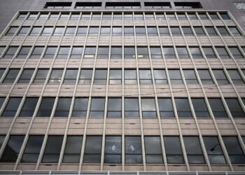 Facade of a modern office building with a grid of square windows framed by vertical and horizontal concrete mullions.