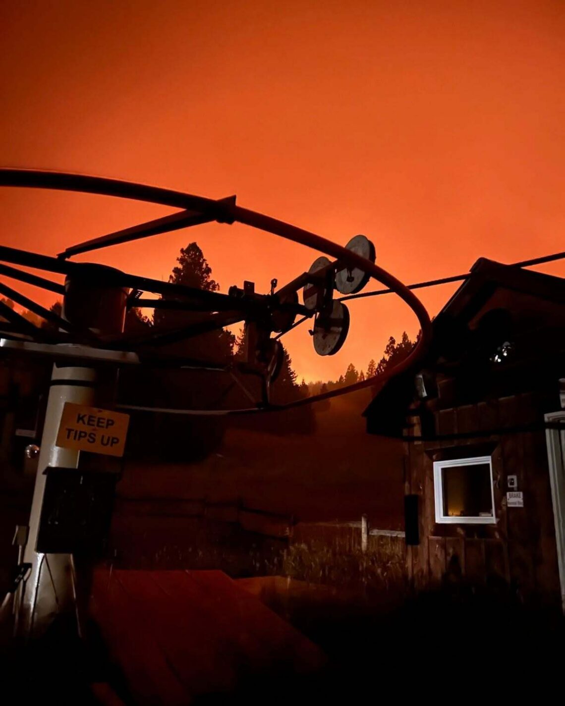 Silhouetted telecom equipment and satellite dishes against an orange smoky sky, with a small building and a 'Keep Tips Up' sign nearby.