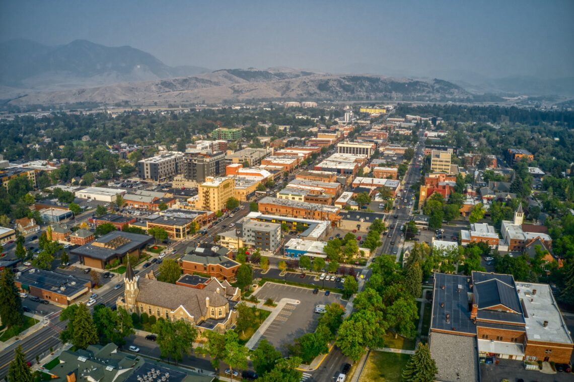 Aerial view of a downtown area with mixed‑use buildings, tree-lined streets, and distant mountains on the horizon.