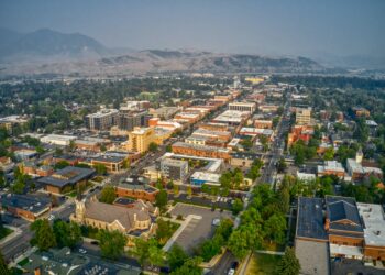 Aerial view of a downtown area with mixed‑use buildings, tree-lined streets, and distant mountains on the horizon.