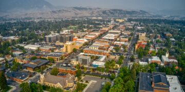 Aerial view of a downtown area with mixed‑use buildings, tree-lined streets, and distant mountains on the horizon.