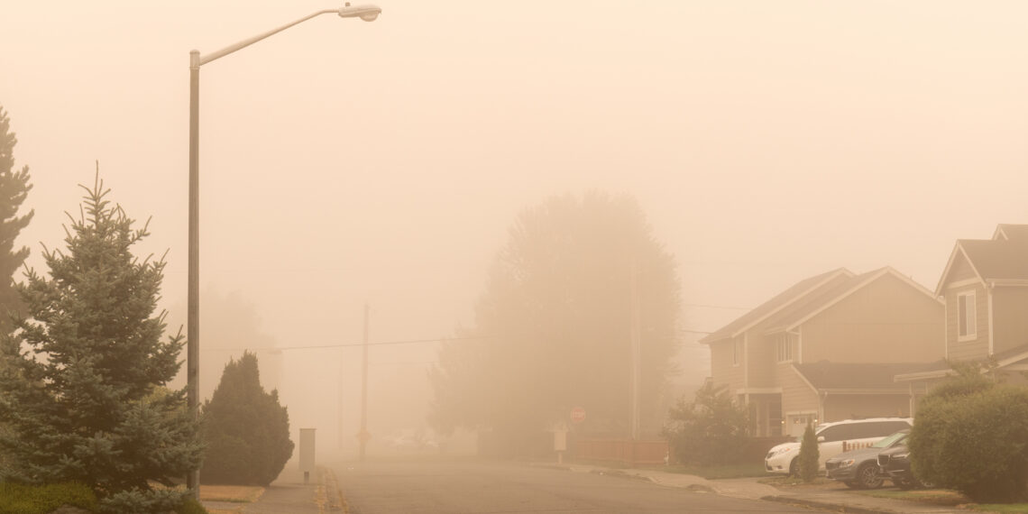Suburban street in dense orange fog with a tall streetlight extending over the road and houses to the right.