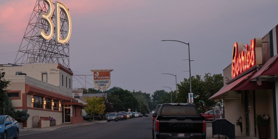 Evening street scene with a large neon '3D' sign atop a framework on the left, and a red neon 'Diners' sign on the right, with parked cars along the street.