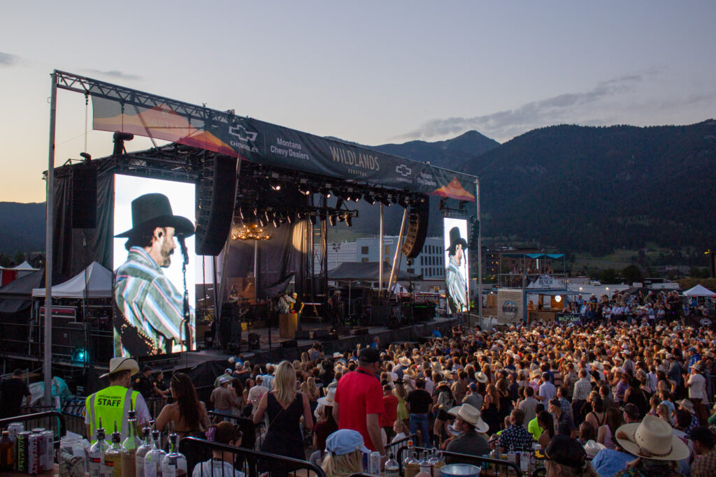Outdoor concert at Wildlands Festival with large stage, banners, and a crowded audience against mountain backdrop at dusk.
